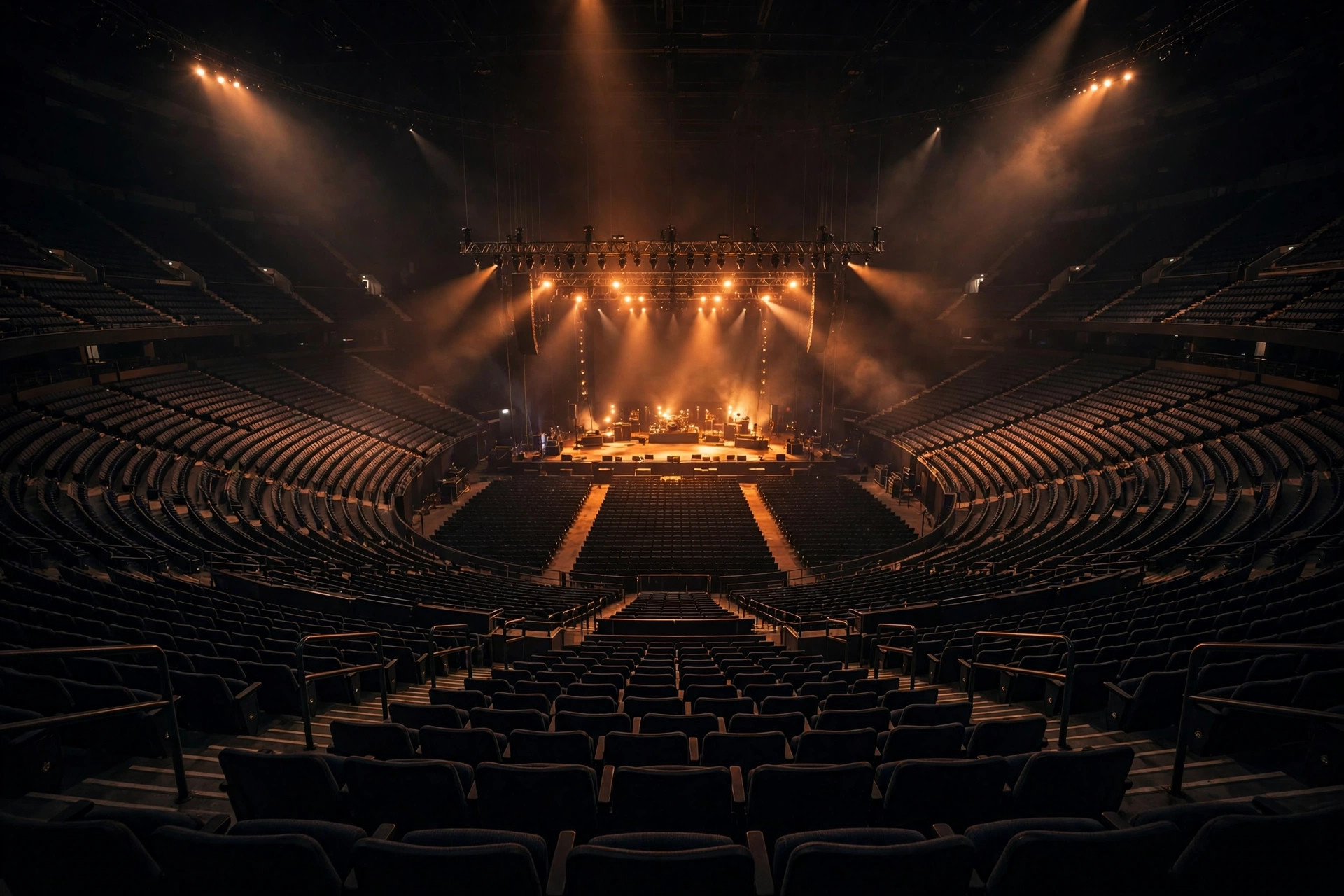 A vast empty arena at night, stage glowing, seats curving into darkness